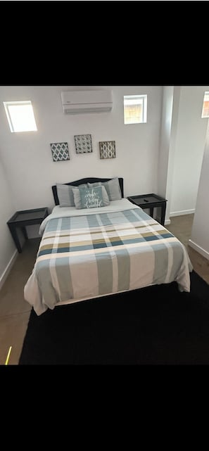 A bedroom with a bed, two nightstands, a window, and a wall-mounted air conditioner.
