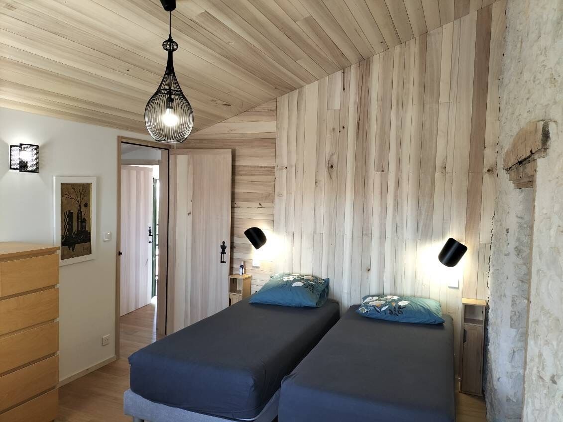 Ett rum med två sängar, träväggar, en hängande lampa och en dörr som leder till ett annat rum.