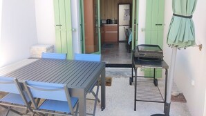 En terrasse med et bord og stole, grill og et køkken, der kan ses gennem en åben dør.