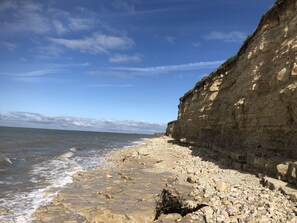 Een rotsachtig strand met een steile klif aan de zijkant en rustige golven die op het strand spoelen.