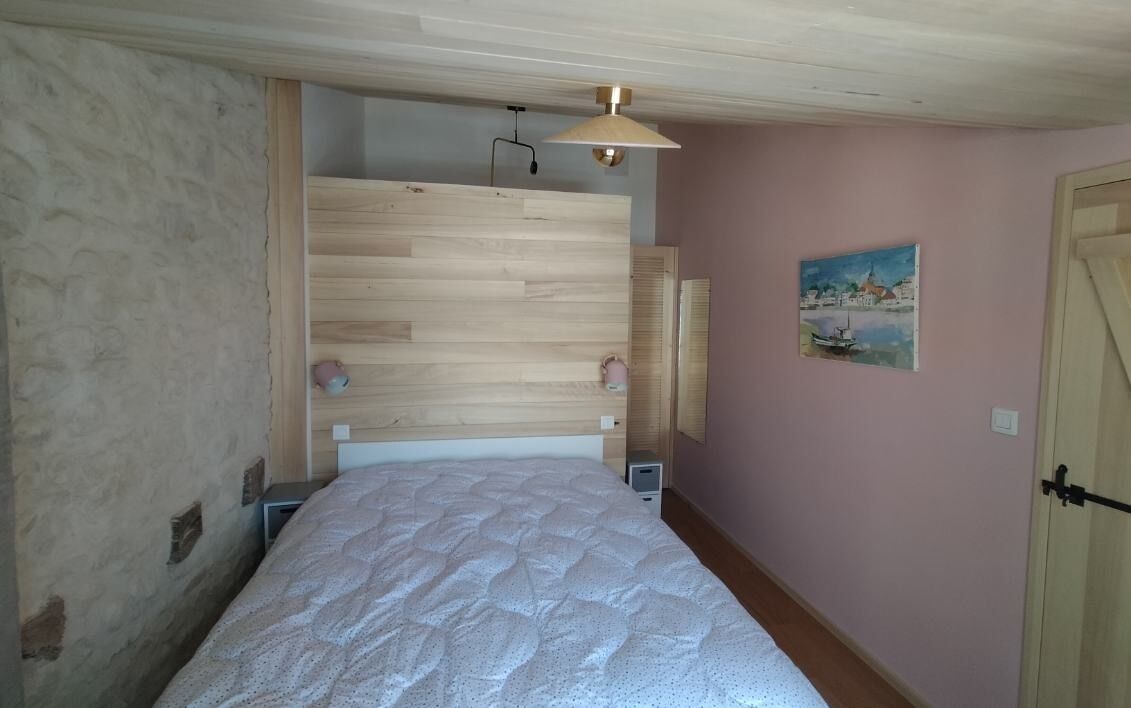 Une chambre à coucher avec une tête de lit en bois, un lit recouvert d’une couette blanche, un tableau accroché au mur et une porte dotée d’une poignée.