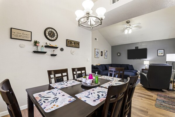 A dining area with a table set for four, surrounded by chairs, and a living area with a sofa and a television.