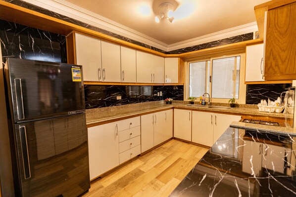 A modern kitchen with black marble countertops, white cabinets, and a black refrigerator.