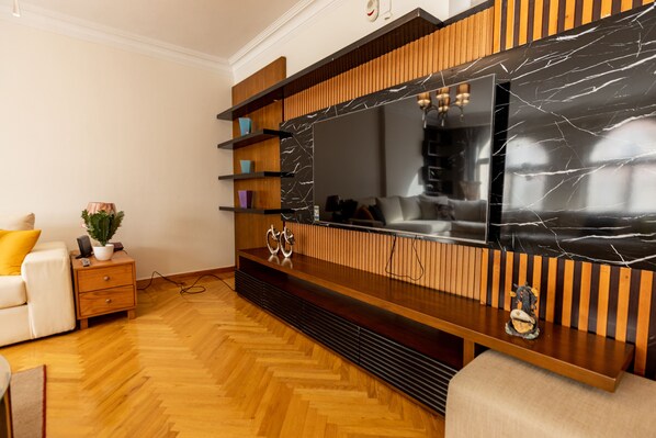 A modern living room with a large flat-screen TV, wooden shelving, and a herringbone-patterned floor.