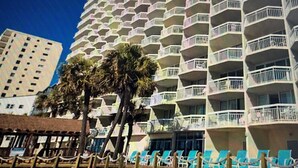 A high-rise hotel with multiple balconies, palm trees, and a beach area with lounge chairs. - Beautiful oceanfront Condo with direct access to the beach, steps from the sand. (Murrells Inlet)