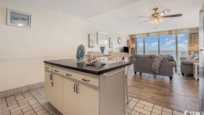 A kitchen with a central island, a ceiling fan, and a large window offering a view of the sky. - Beautiful oceanfront Condo with direct access to the beach, steps from the sand. (Murrells Inlet)