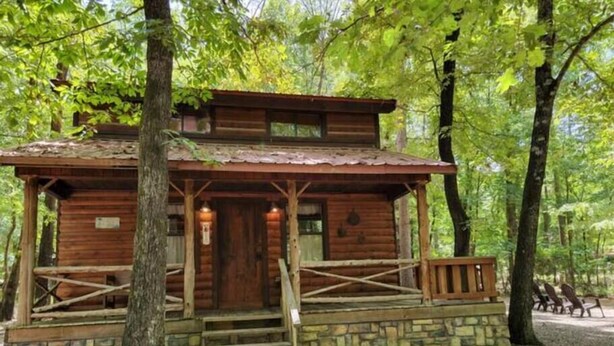 A wooden cabin with a porch, a staircase, and a stone foundation.