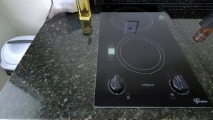 Una cocina con tope de inducción negro, una botella de aceite y un electrodoméstico blanco sobre la encimera.
