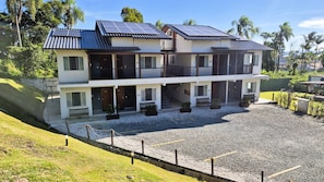 A two-story building with solar panels, a gravel driveway, and a fenced courtyard. - Ipê Eco Village, Apartamentos com cozinha perto da Praia e do Beto Carrero (Penha)