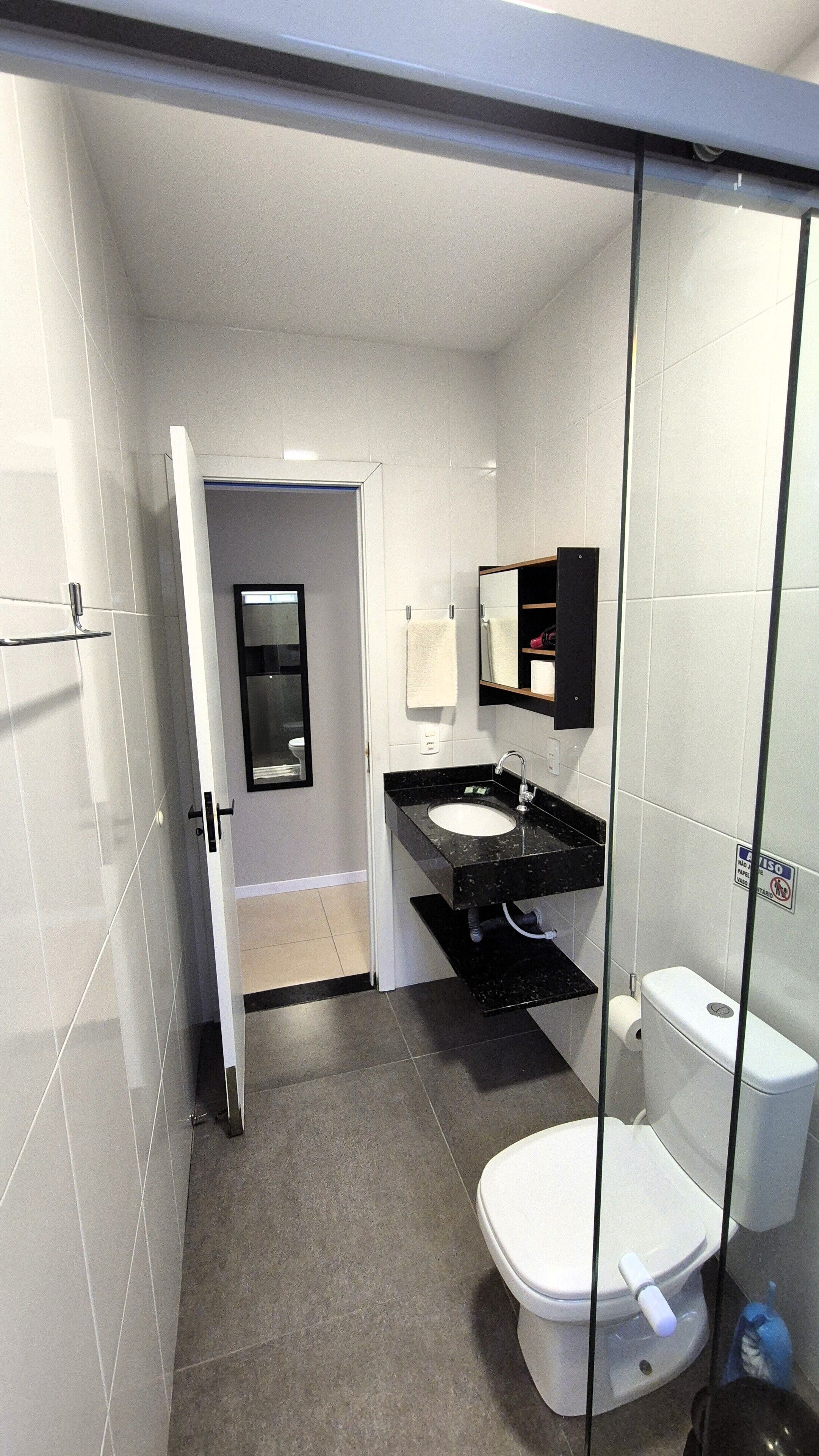 Un baño moderno con mampara de vidrio, inodoro blanco, lavamanos y espejo.