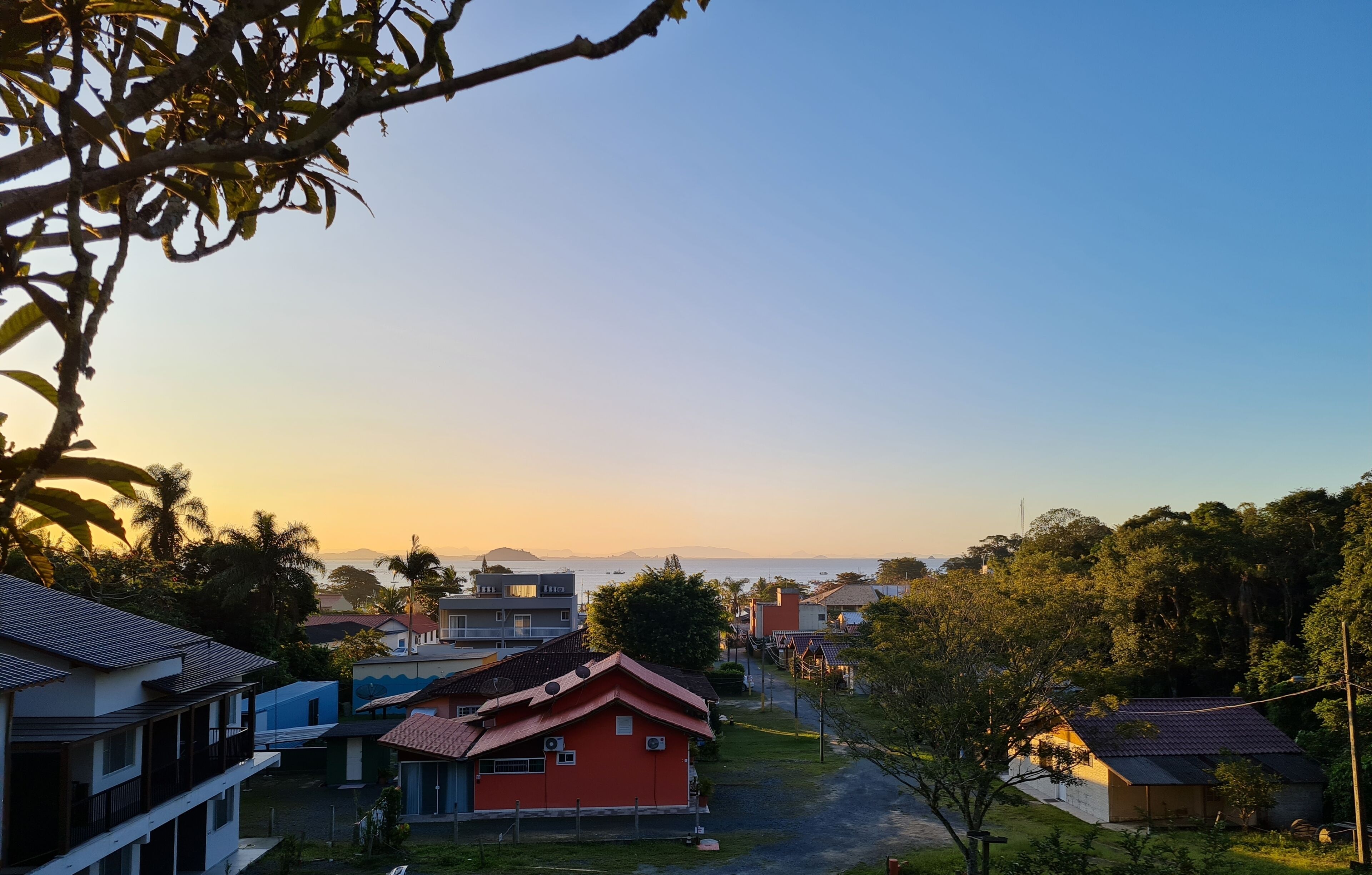 Un barrio residencial con casas, cielo despejado y vista distante al mar.