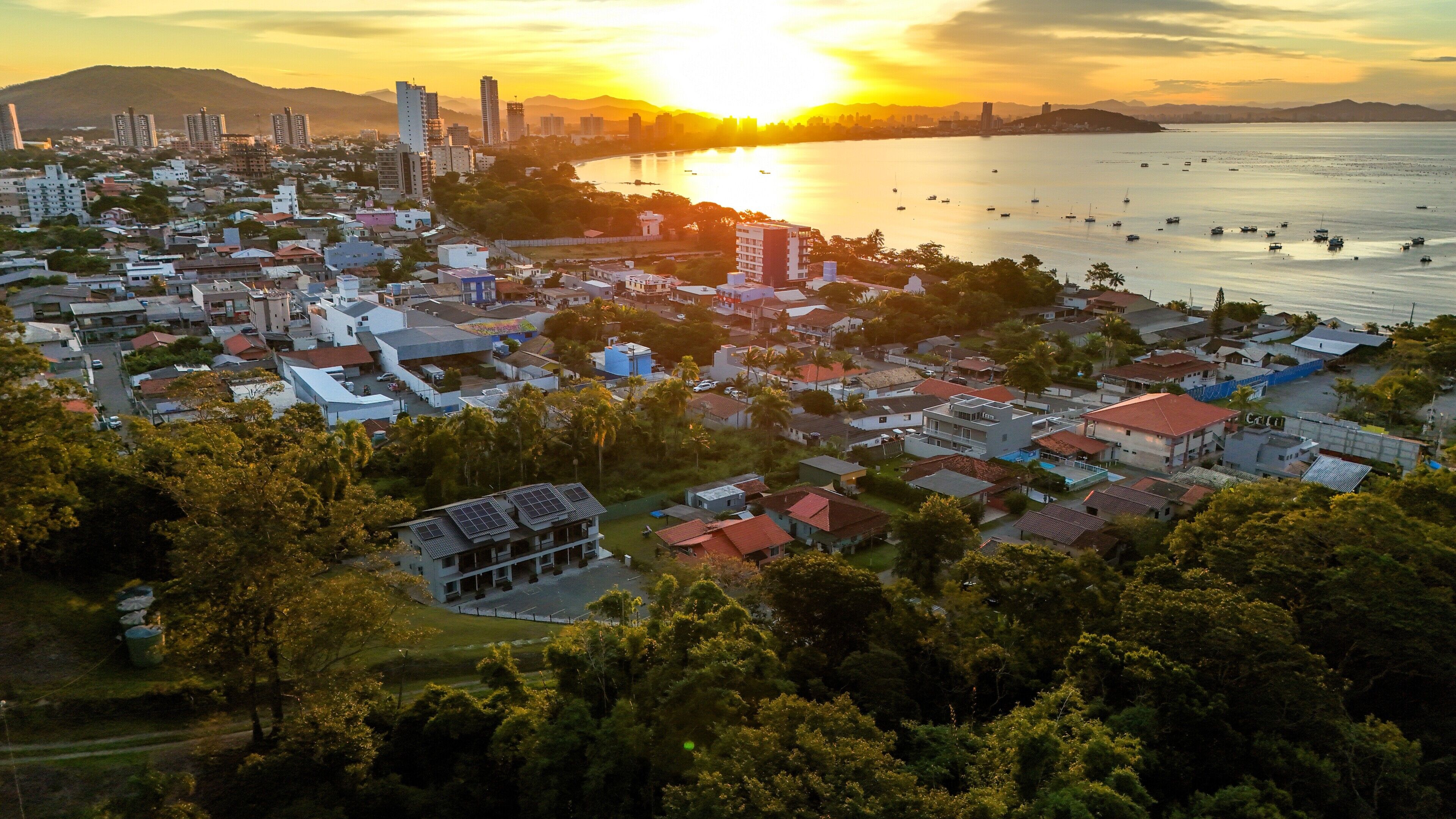 A coastal cityscape with residential buildings, a marina, and a sunset.