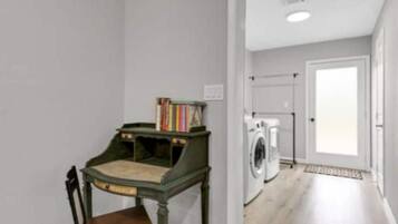 Una habitación con una pequeña mesa y una silla, una lavadora y una puerta que da a otra habitación.