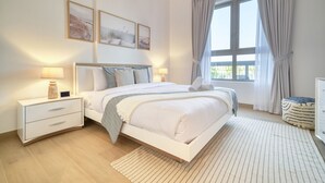 A modern bedroom with a large bed, bedside tables, a window with curtains, and artwork on the wall. - Placid 1BR at La Cote 5 Palm Jumeirah by Deluxe Holiday Homes (Dubai)