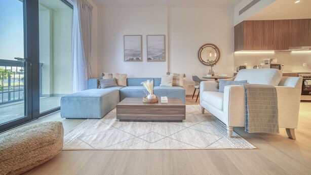 A modern living room with a sectional sofa, a coffee table, and a view to the outside. - Placid 1BR at La Cote 5 Palm Jumeirah by Deluxe Holiday Homes (Dubai)