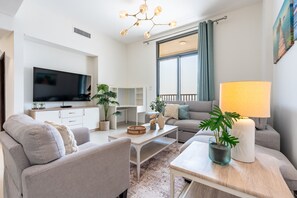 A modern living room with a flat-screen TV, grey sofas, a coffee table, and a chandelier.
