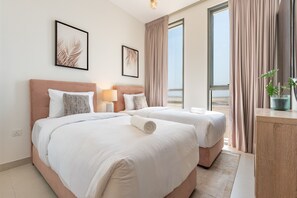 Een hotelkamer met twee bedden, een nachtkastje, een lamp en uitzicht op het strand.