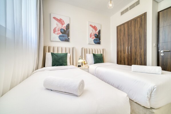 A hotel room with two beds, a large wooden wardrobe, and two framed floral paintings on the wall.