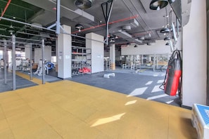 Une salle de sport spacieuse, équipée de divers appareils d’exercice, notamment des tapis de course et des appareils de musculation, et dont le sol est recouvert de carreaux jaunes.