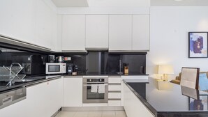 Una cucina moderna con mobili bianchi, un piano di lavoro nero, un forno a microonde, una macchina da caffè e un fornello.