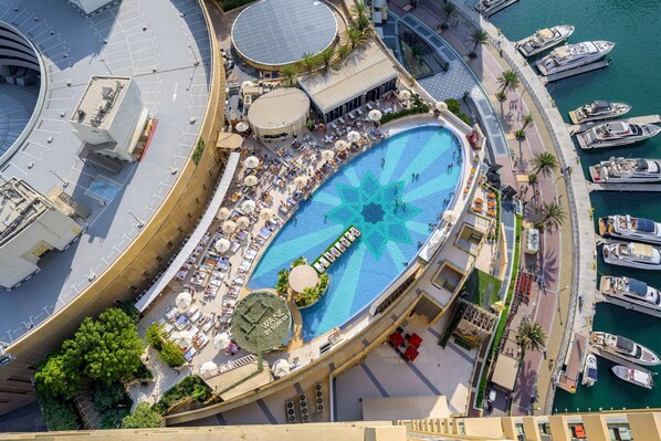 An aerial view of a hotel with a large pool, outdoor seating, and boats docked nearby.