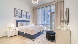 A modern bedroom with a large bed, a nightstand, a dresser, and a view of the city through large windows.