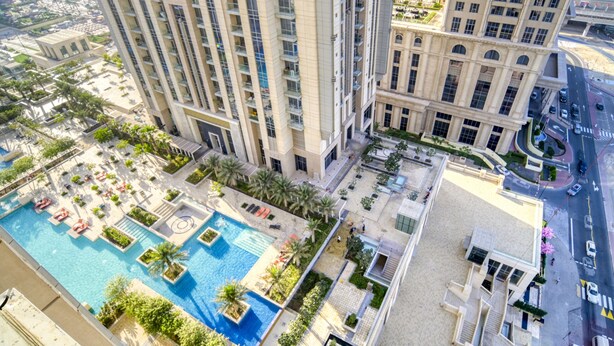 A high-rise building with a rooftop pool area, multiple balconies, and a landscaped courtyard.
