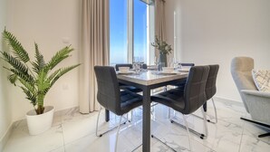 A dining area with a table set for four, a potted plant, and a view through a large window.