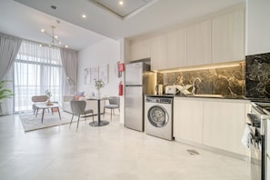 A modern kitchen with a built-in washer and dryer, a dining area with a table and chairs, and a large window with sheer curtains.