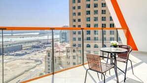 A balcony with a glass railing, a table with two wicker chairs, and a view of a cityscape including a tall building and a bridge. - Spectacular 1BR at Binghatti Avenue Al Jaddaf by Deluxe Holiday Homes (Dubai)