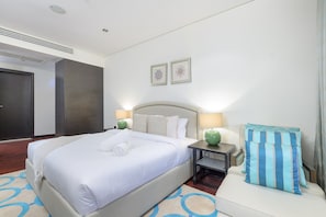 Une chambre d’hôtel avec un grand lit, des tables de chevet avec des lampes, une tête de lit et un petit coin salon avec un coussin.