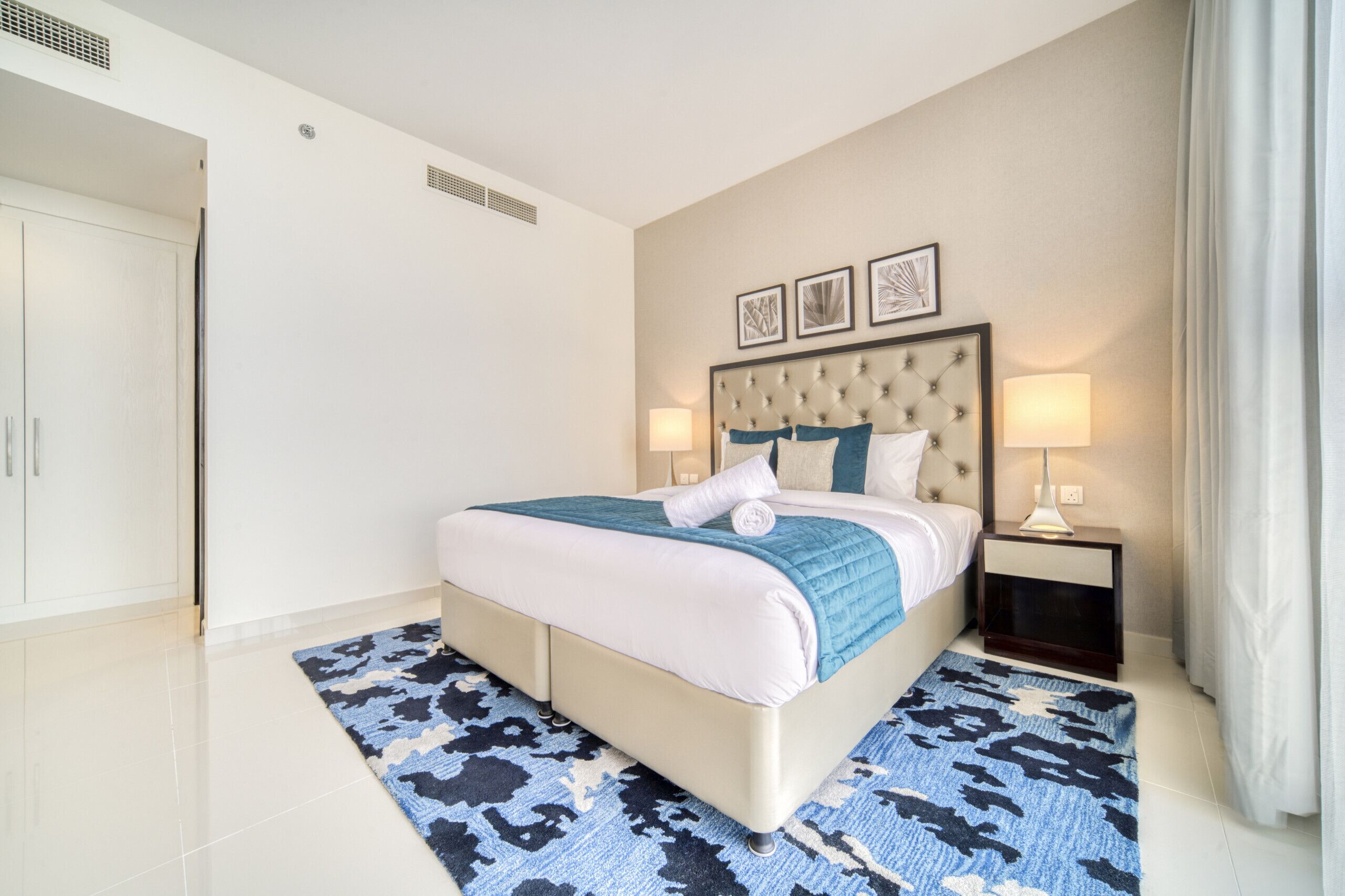 A modern hotel room with a large bed, a bedside table with a lamp, and a view of the hallway.