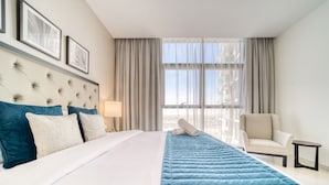 A hotel room with a large bed, a chair, a small table, and a window with curtains.