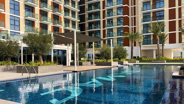 A modern hotel with a swimming pool, outdoor seating, and palm trees.