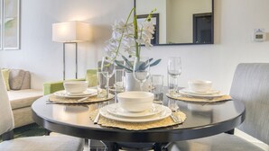 A dining table set with white bowls, plates, and cutlery, surrounded by chairs, with a vase of white orchids in the center.