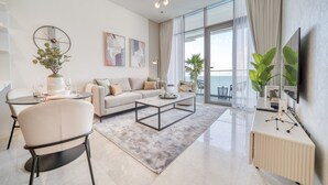 Ein modernes Wohnzimmer mit Sofa, Couchtisch und Sesseln, ein großes Fenster mit Vorhängen und eine Pflanze auf der Fensterbank.