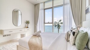 Ein Hotelzimmer mit einem großen Bett, einem Nachttisch, einem Spiegel, Blick auf den Ozean und einem Vorhangfenster.