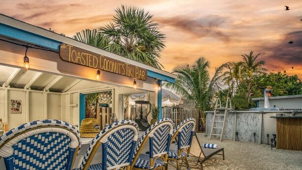 En tiki bar med udendørs siddepladser og et skilt, der siger "The Toasted Coconut's Tiki Bar".