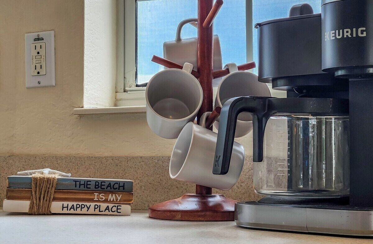 A kitchen with a Keurig coffee maker, a mug rack, and a stack of books on the counter.