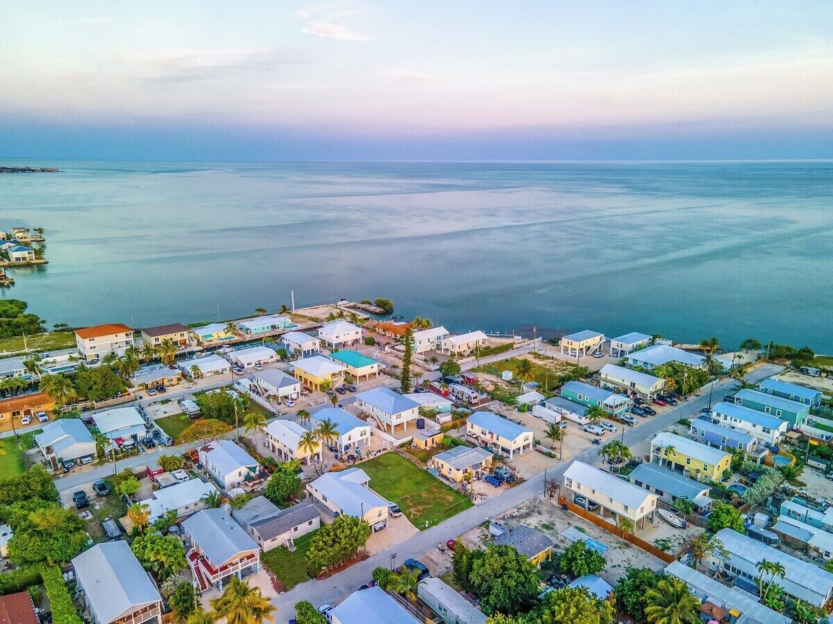 An aerial view of a coastal residential area with houses, roads, and a marina.