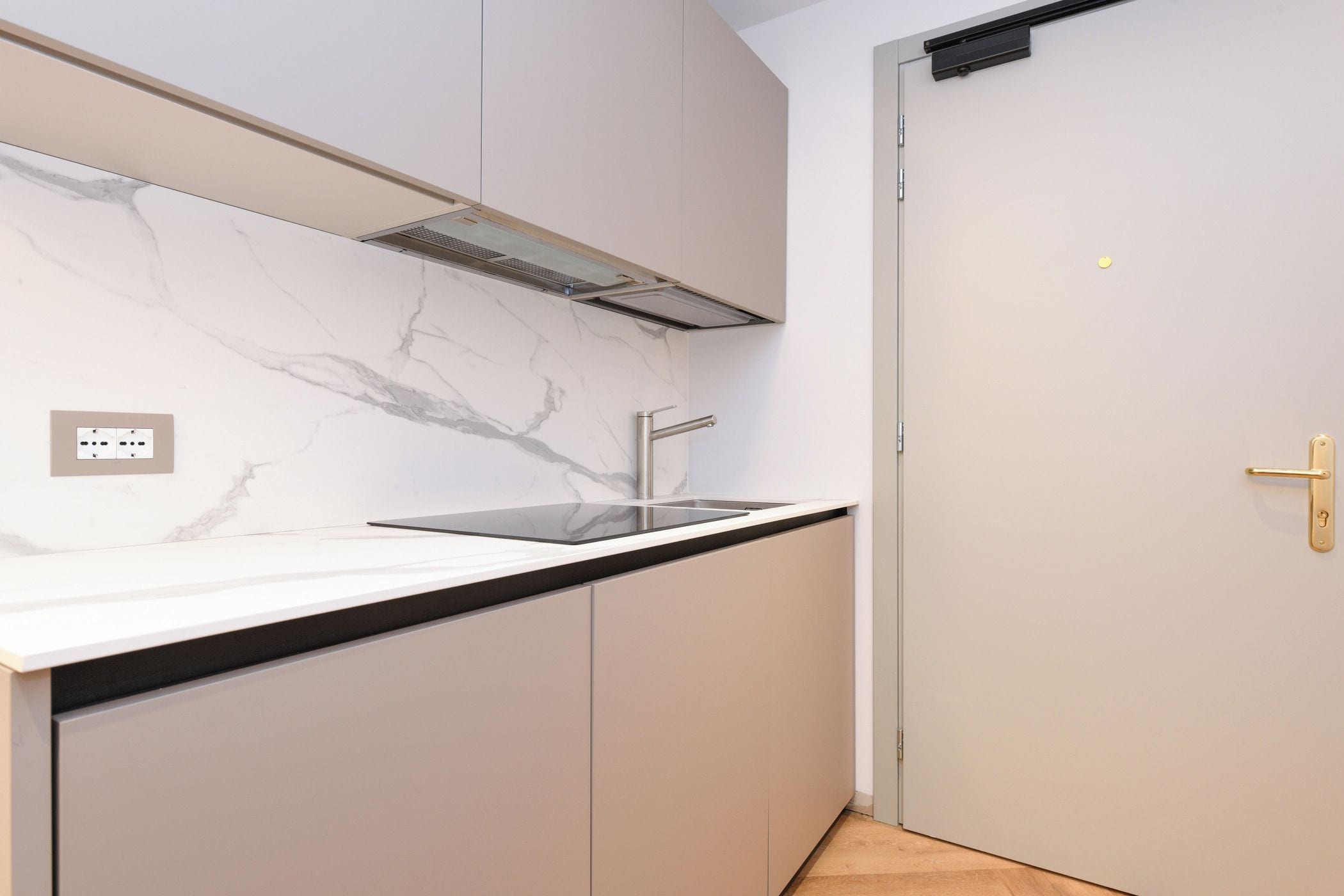A modern kitchen with a marble backsplash, stainless steel sink, and light-colored cabinets.