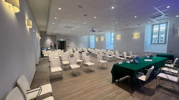 A conference room with rows of chairs, a long table, and a projector screen.