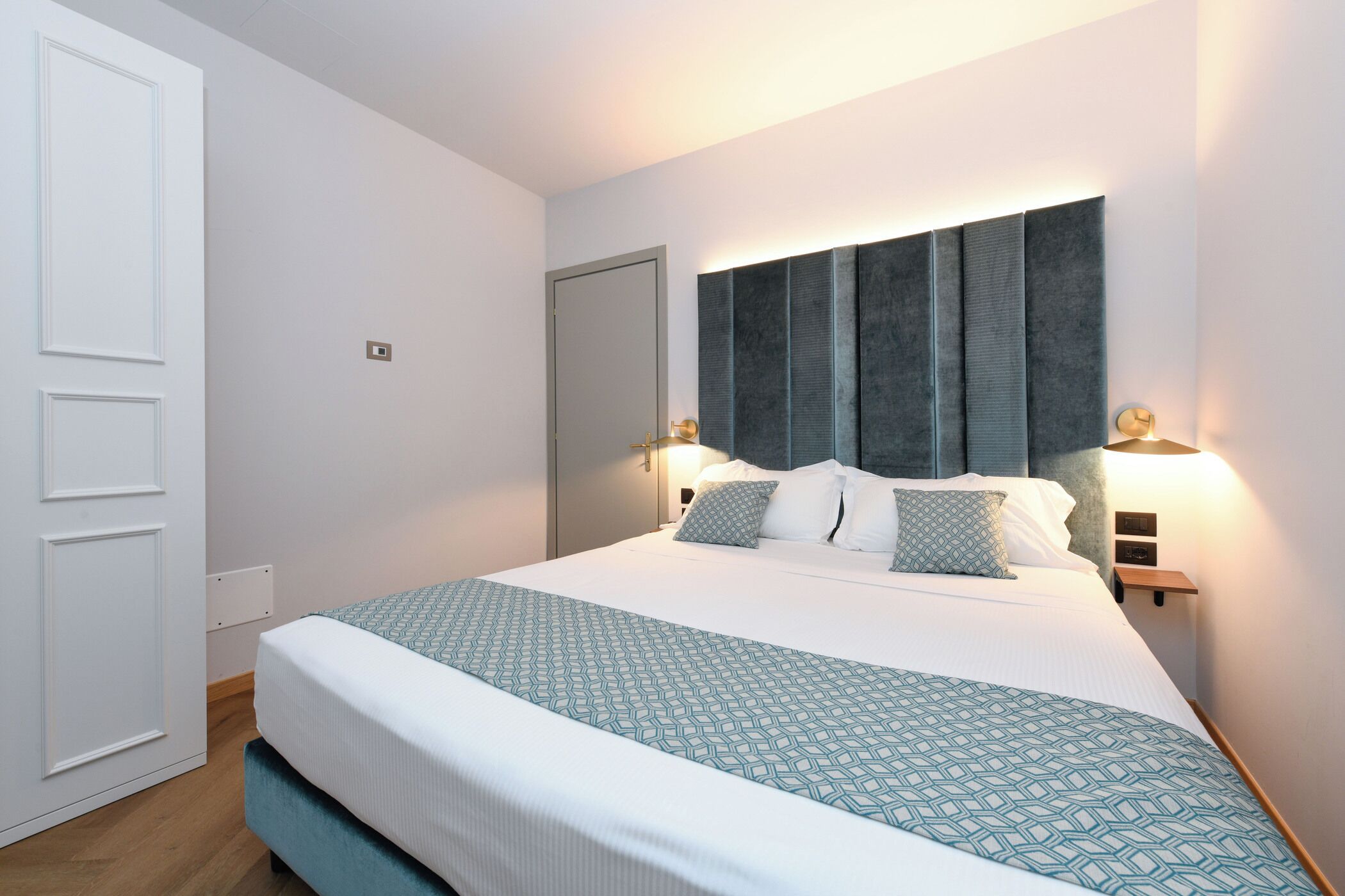 Ein ordentlich eingerichtetes Hotelzimmer mit einem großen Bett, einem Nachttisch und einer Wandleuchte.