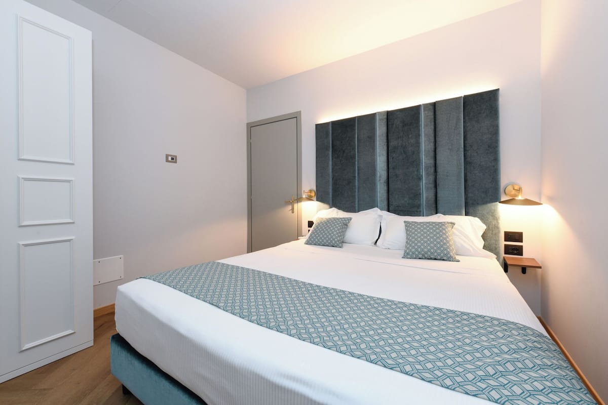 A neatly arranged hotel room with a large bed, a bedside table, a nightstand, and a wall-mounted light fixture.