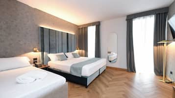 Ein modernes Hotelzimmer mit einem großen Bett, einem kleineren Bett, einem Nachttisch mit Lampe, einem Spiegel und einem großen Fenster mit Vorhängen.
