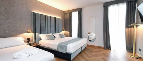 A modern hotel room with a large bed, a smaller bed, a bedside table with a lamp, a mirror, and a large window with curtains.
