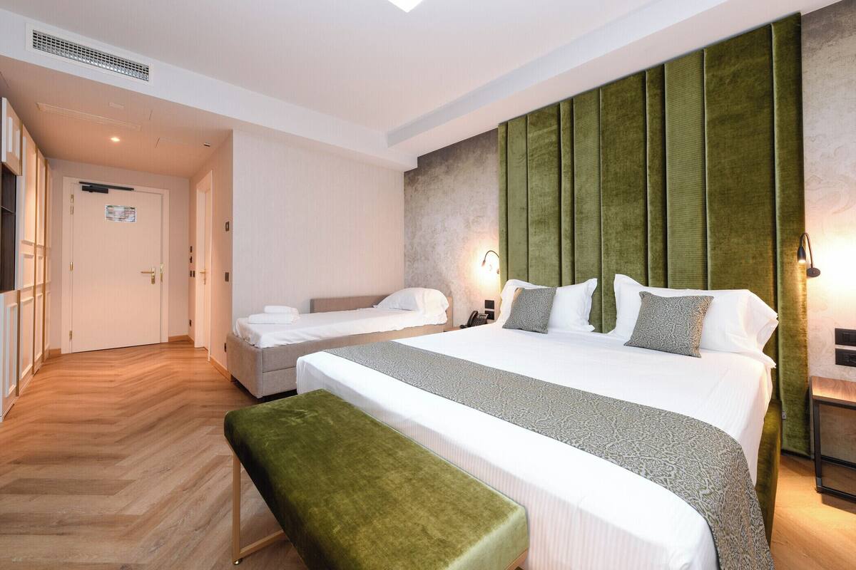 A hotel room with a large bed, a smaller bed, a bench, a desk, and a wardrobe.