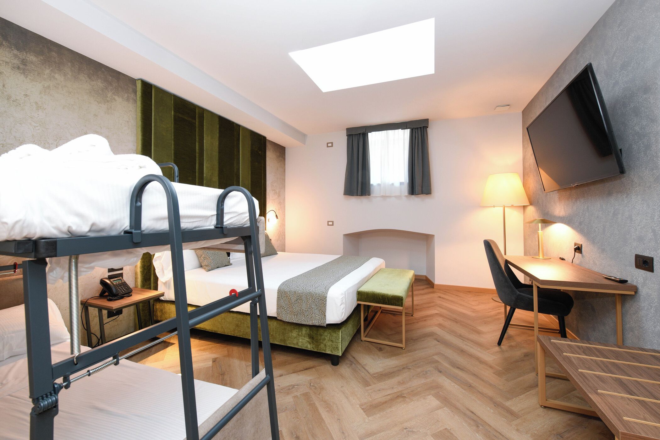 A hotel room with bunk beds, a desk, a chair, a TV, and a window with curtains.