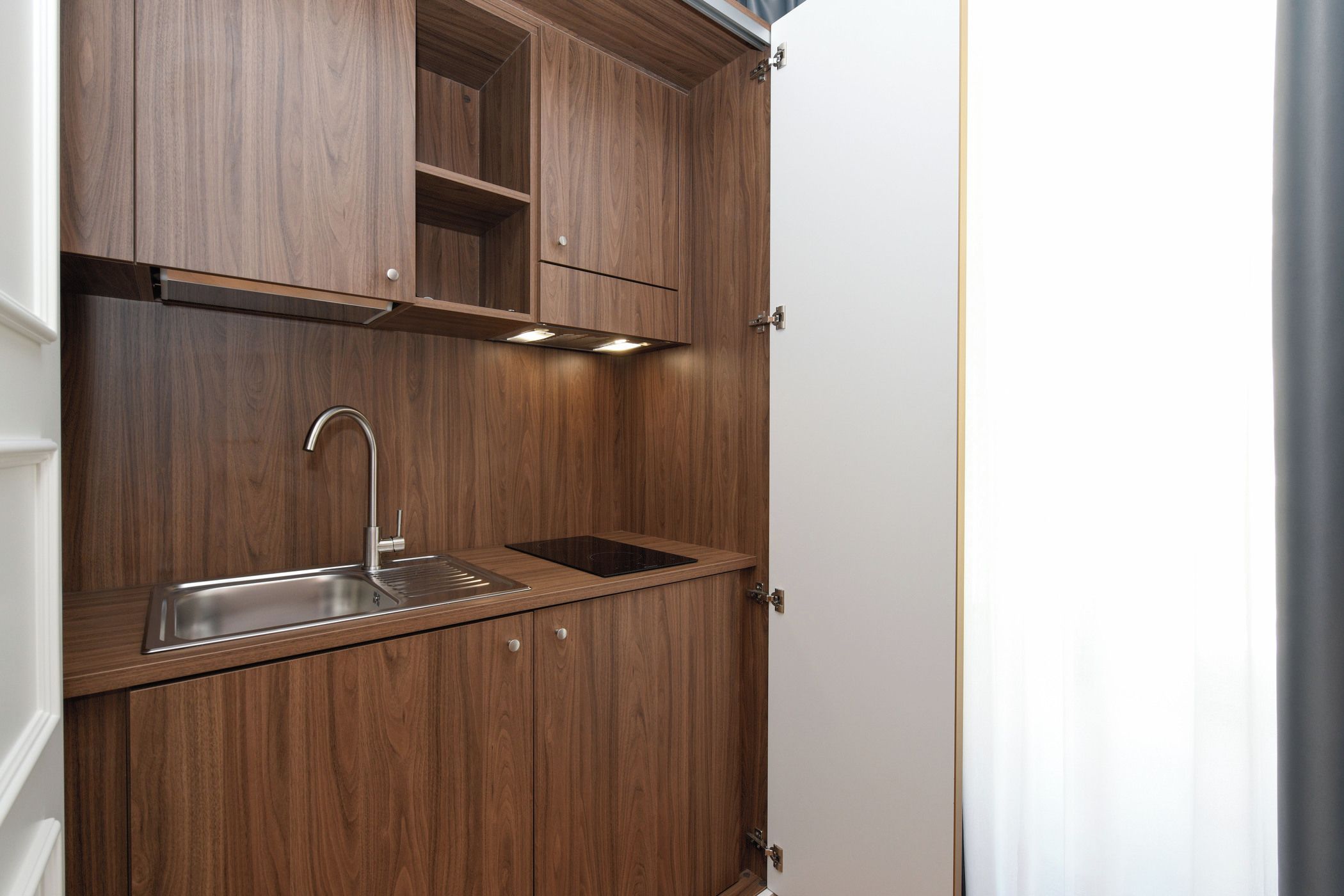 A compact kitchen with wooden cabinetry, a stainless steel sink, and under-cabinet lighting.