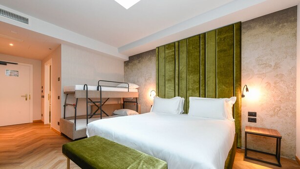 Ein Hotelzimmer mit Etagenbett, einem Einzelbett, einer grünen Bank und einem kleinen Tisch.